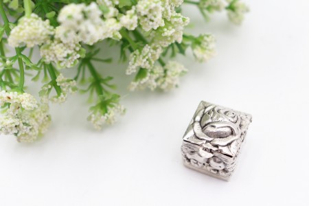 Caixa de comprimidos em prata e forma de cubo profusamente relevada